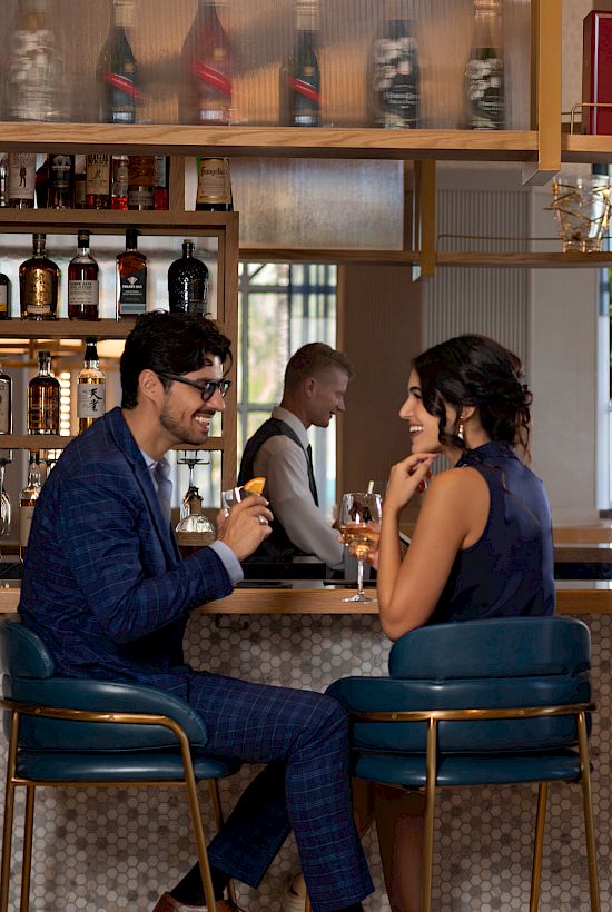 People enjoying drinks and conversation in a stylish bar, featuring elegant decor and a selection of spirits on display.