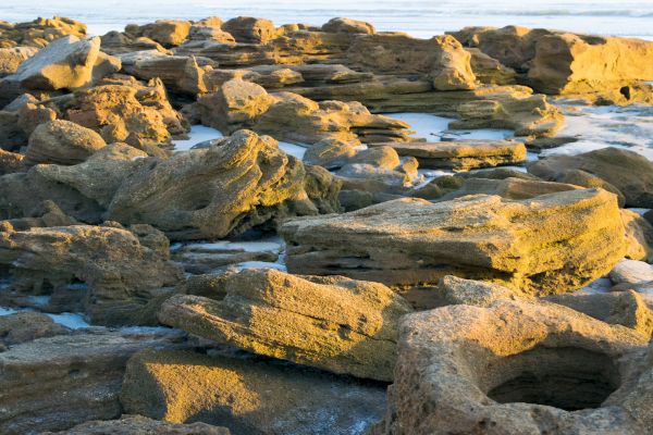 The image shows a rugged, rocky coastal area with large rocks warmed by sunlight near the ocean's edge.